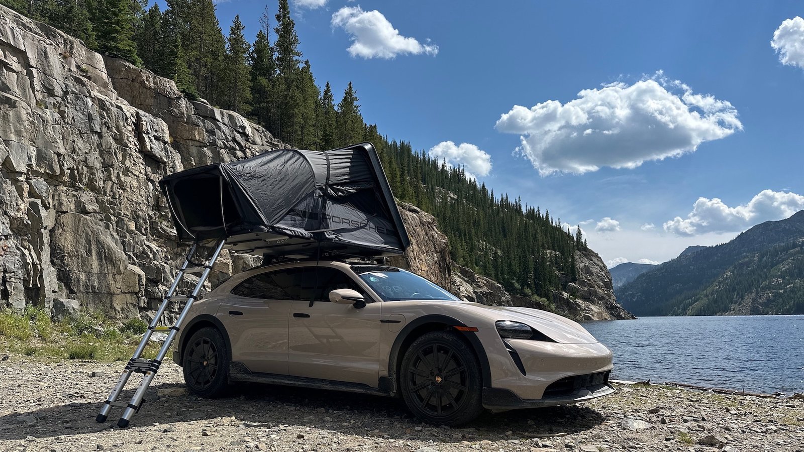 an SUV with a pop tent on top and a ladder in front of a mountain lake