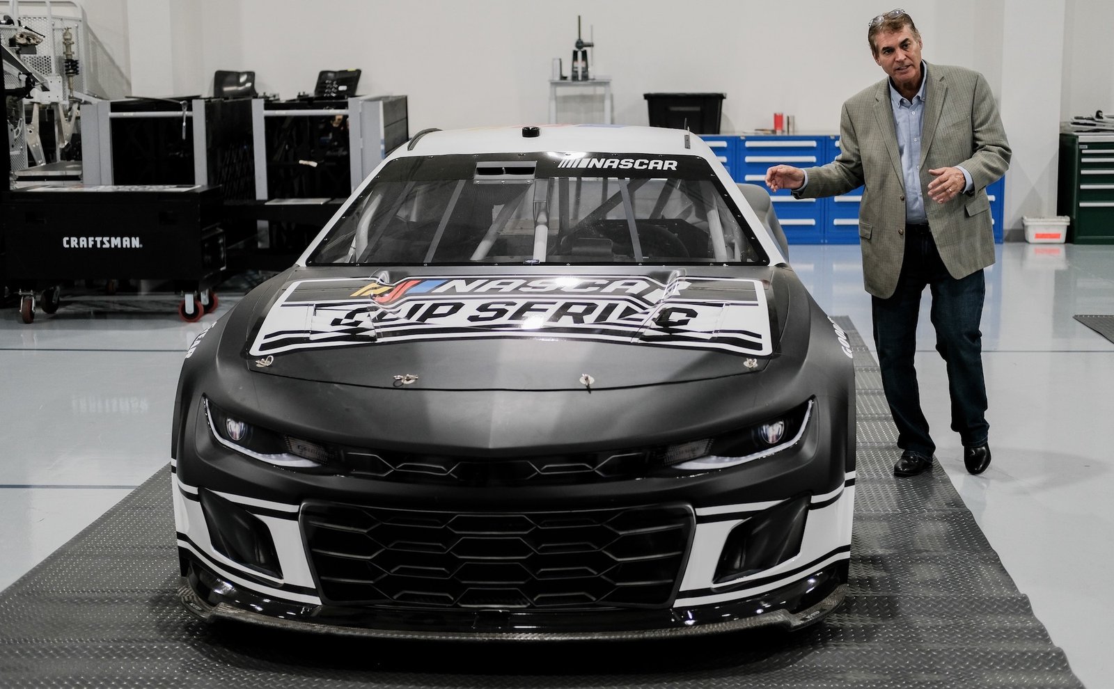 a car with "NASCAR" on hood parked inside a facility with man standing outside of car