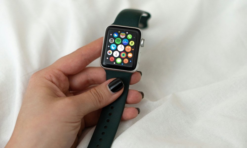person holding Apple Watch over bed sheets