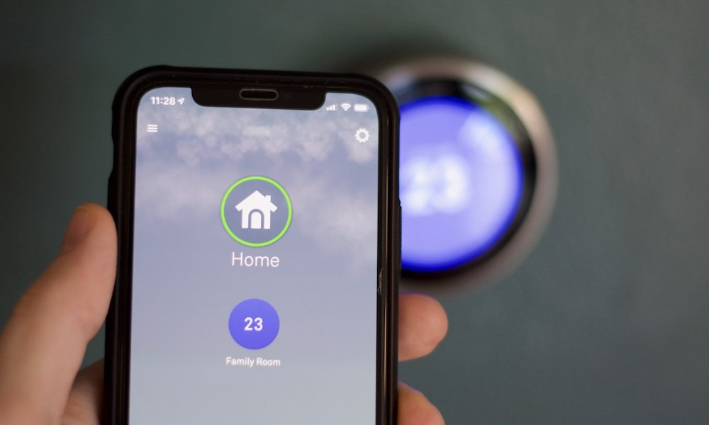 Cell phone and hand adjusting temperature on smart thermostat